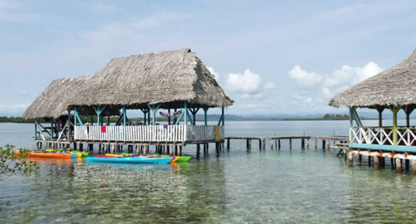 Stilt structures stand over shallow water, with colorful watercraft docked to them